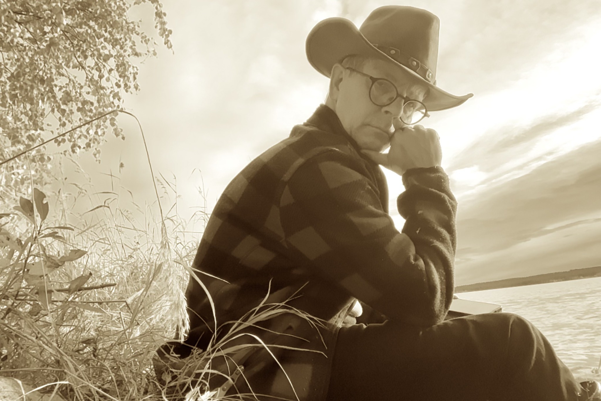 Aaron Hakso in a hat and glasses, sitting by the lakeshore